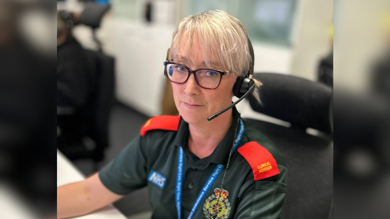 Kate - a lady with blonde hair and glasses sat at a desk wearing a headset.