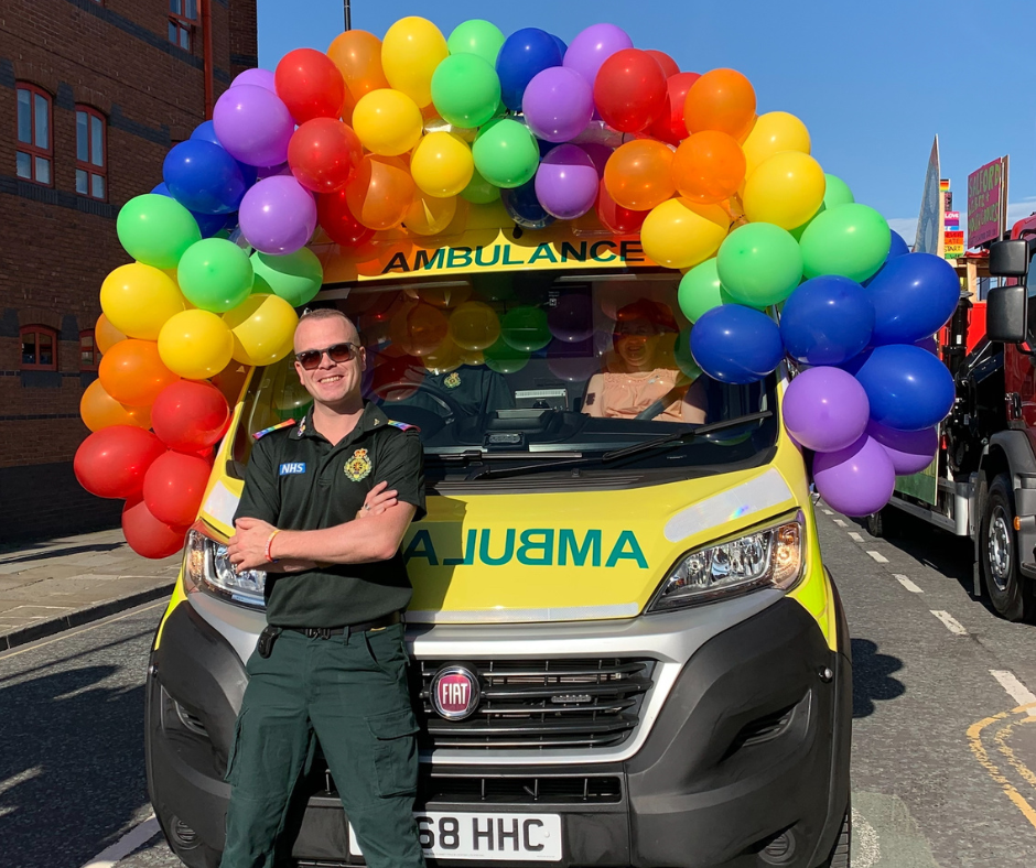 Paramedic standing in front of an ambulance that has rainbow coloured balloons on top