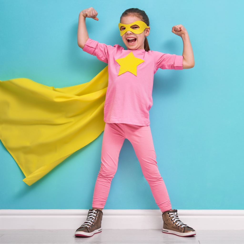 A child dressed in pink with a yellow cape, mask and star in a superhero pose