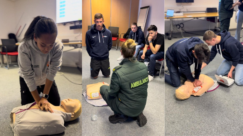 This image is a triptych showing three scenes from a first aid training session. From left to right: the first panel displays a person practicing CPR on a training manikin on the floor. The middle panel shows an instructor observing three participants, two sitting and one kneeling looking towards the instructor. The third panel depicts two participants kneeling, as they practice using an Automated External Defibrillator (AED) on a training manikin. Each scene is set in an indoor environment, likely a classroom or a training facility, emphasising hands-on medical training.