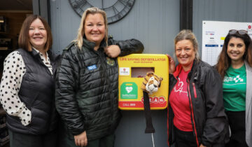 Three women stood in line with a defibrillator in the middle.