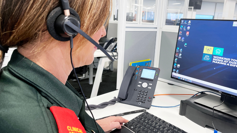 An individual in a green uniform with 'Clinical Advisor' badge working at a computer desk, wearing a headset, with text promoting support sessions for urgent and emergency care roles.