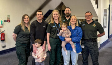 A group of emergency service workers standing with a woman holding a baby and a man hugging a small boy.