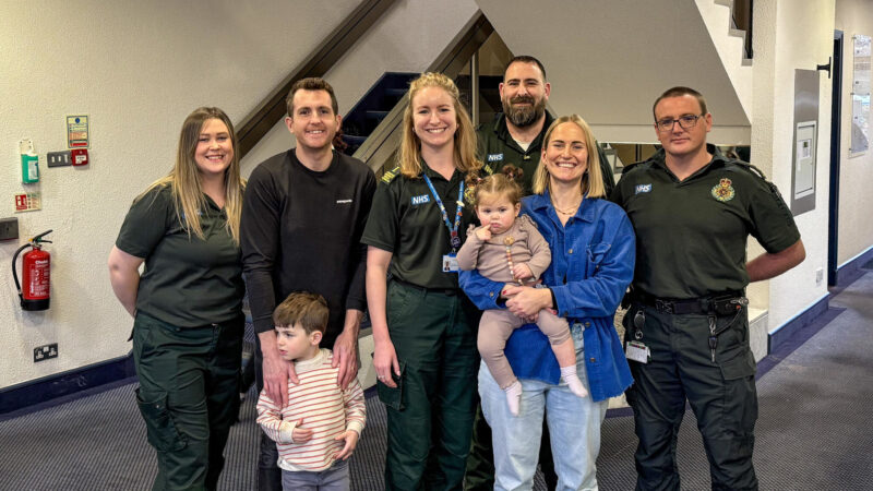 A group of emergency service workers standing with a woman holding a baby and a man hugging a small boy.