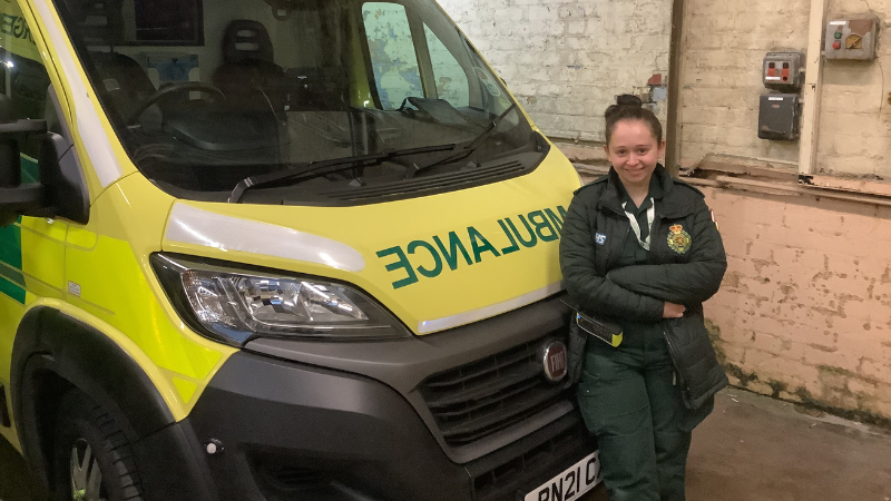 Paramedic Lucy stands in front of a parked ambulance.