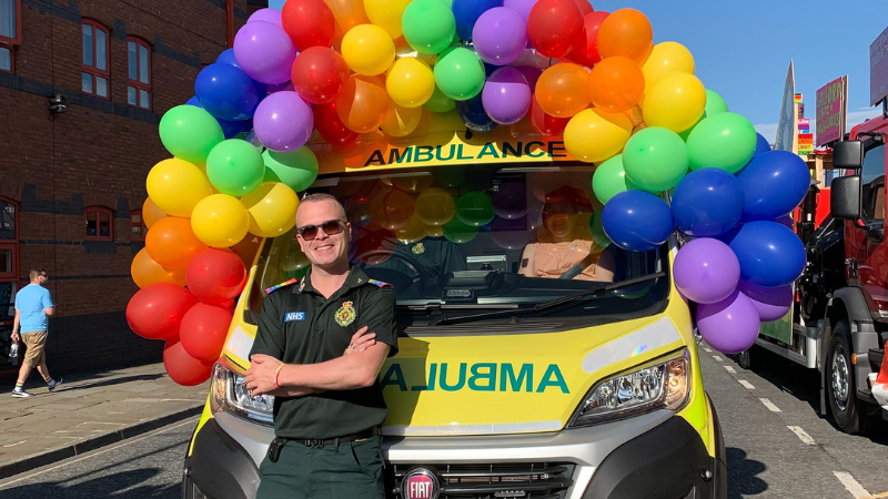 Paramedic standing in front of an ambulance that has rainbow coloured balloons on top