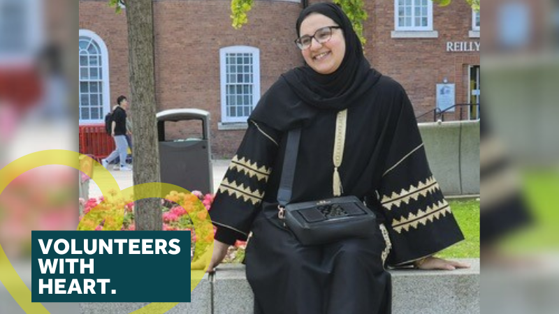 Hadil - a lady with glasses sat on a wall smiling at the camera