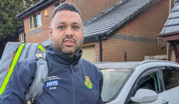 A community first responder carrying his kit bag standing in front of a residential building.